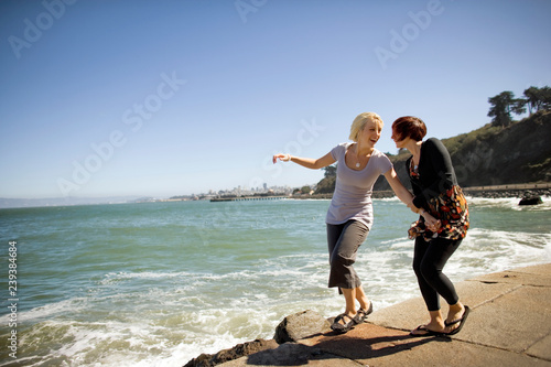 Two young women having fun together on a footpath next to a beach.