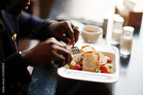 Close up hands of fashionable african american man in suit sitting at cafe and eating salad.