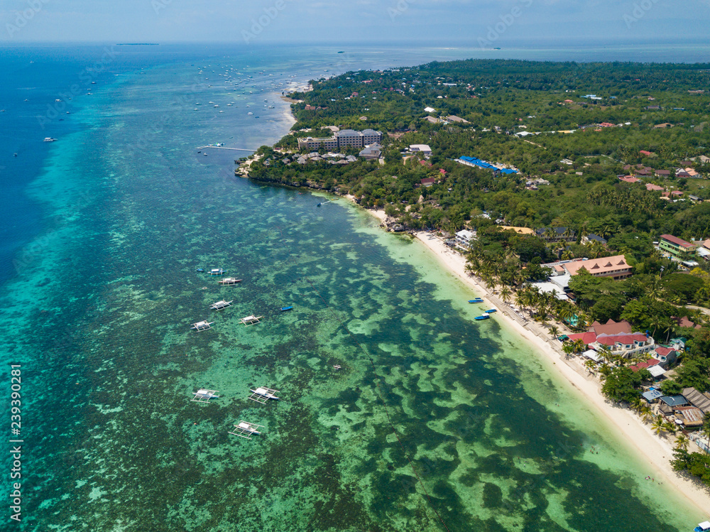 Aerial drone view of Alona beach at Panglao island. Beautiful tropical island landscape with traditional boats, sand beach and palm trees. Bohol, Philippines.