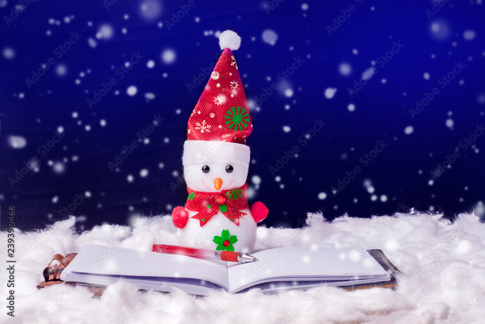 Toy snowman in front of an open book. Fiction reading. Snowman on a dark background during the snowfall. Happy Christmas and New Year's greetings_