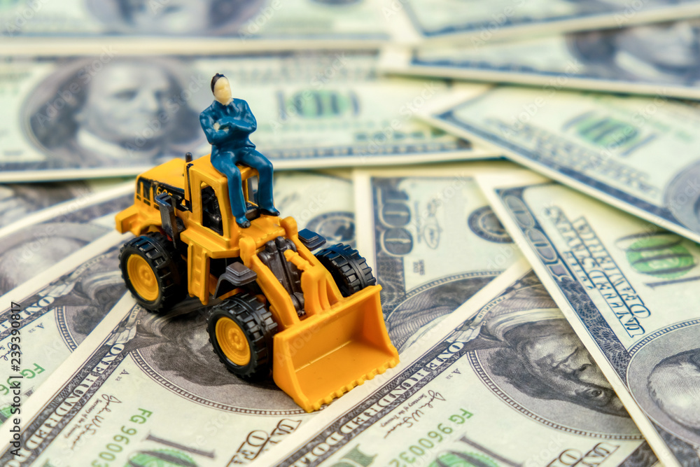 Man sitting on construction vehicle on dollar bill background. Concept of a successful businessman developer