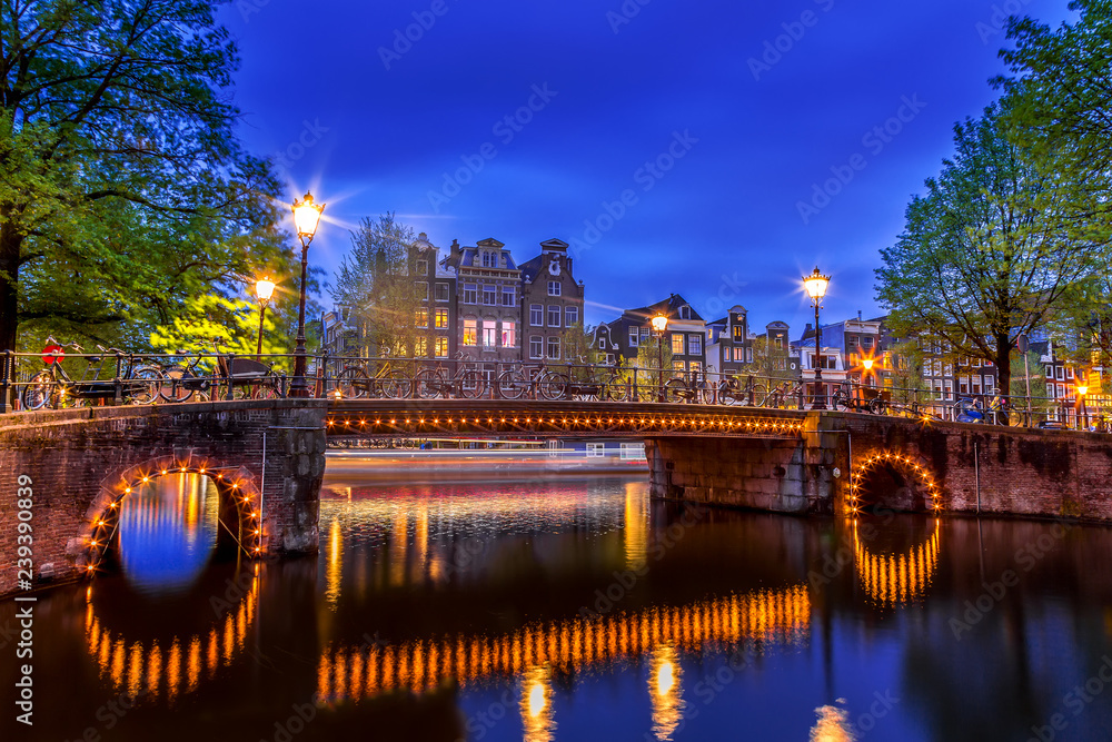 Amsterdam canal with typical dutch houses and illuminated bridge during twilight blue hour in Holland, Netherlands. Picturesque in Holland