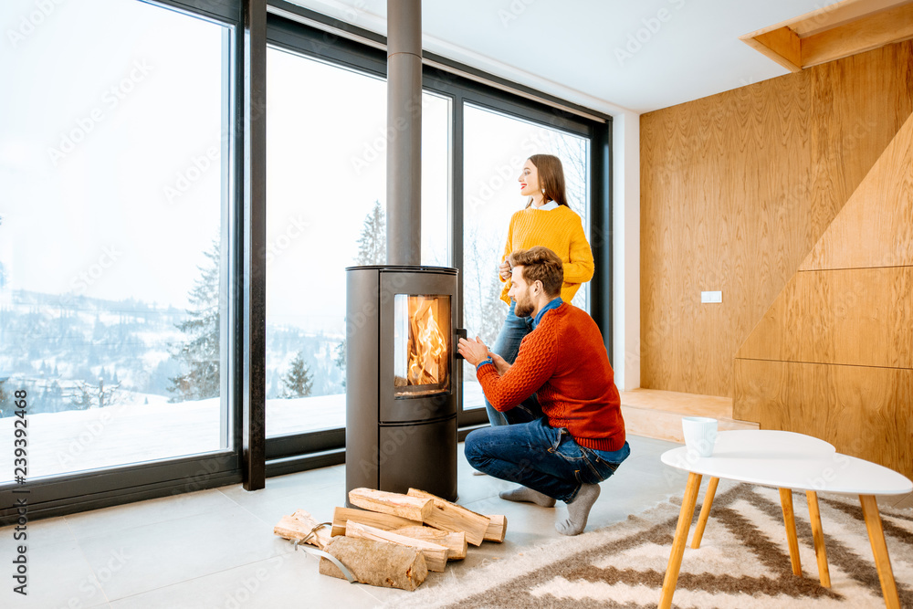Young couple dressed in bright sweaters warming up near the fireplace in the modern house in the mountains during the winter Young couple dressed in bright sweaters warming up near the fireplace in the modern house in the mountains during the winter
