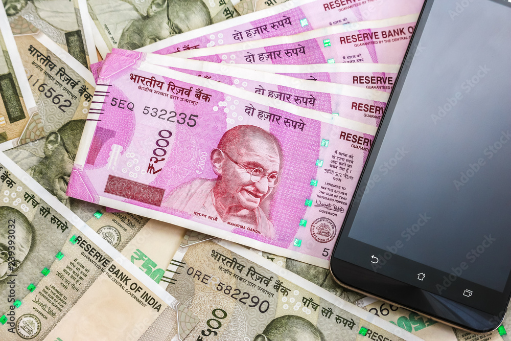 Fototapeta premium Close up view of brand new indian 2000 rupees banknotes and smarthphone. 500 rupee banknotes in background.