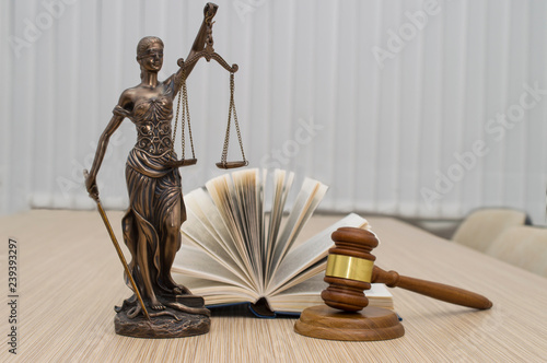 statue of justice, judge's hammer behind books on a wooden table