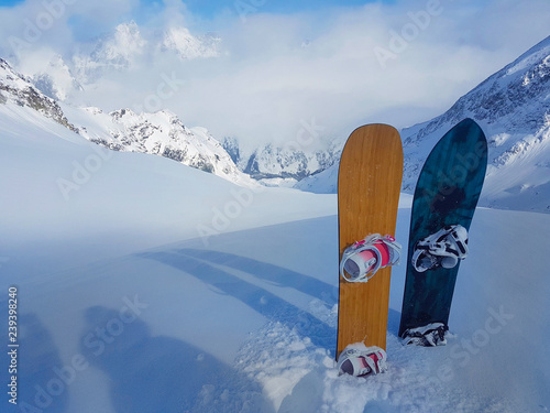 Two snowboards are stuck in the high powder snow at the top of the mountain.