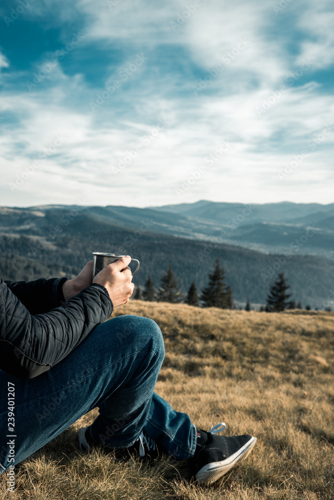 a man with a metal cup sits on a background of mountains a man with a metal cup sits on a background of mountains