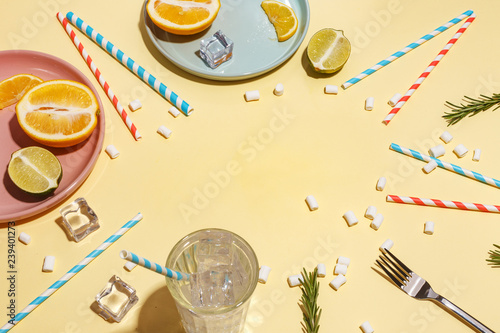 Drink with ice with paper cocktail tubes and fruit on a yellow background. Table setting.