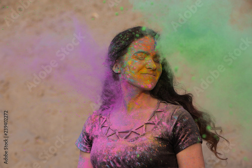 Wonderful brunette model with long wavy hair having fun with purple and green dry Holi powder at the desert