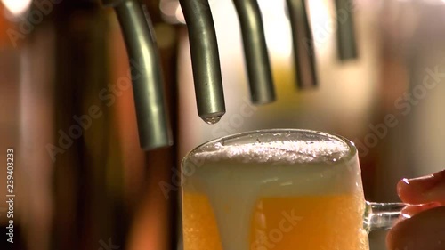 Overflowing glass of beer under tap. Tap beer dripping, slow-mo. photo