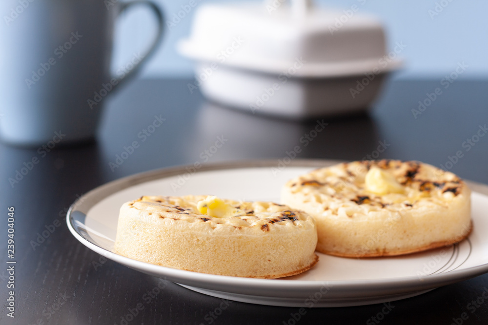 Two hot buttered crumpets on a white plate Two hot buttered crumpets on a white plate