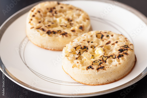 Close-up view of two hot buttered crumpets on a white plate