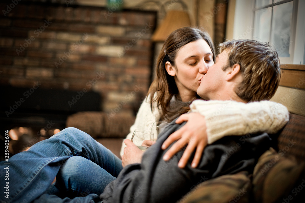 Young couple kissing while seated next to a fire inside their home. Young couple kissing while seated next to a fire inside their home.