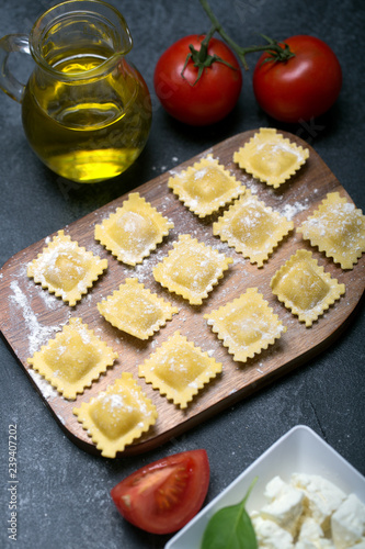 Raw ravioli with basil, cheese and tomatoes on black background