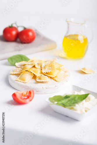 Boiled ravioli with basil, cheese and tomatoes on white table