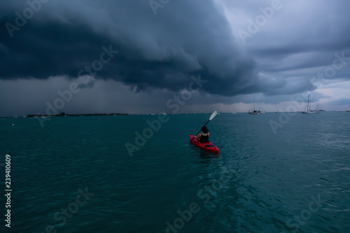 Adventurous girl on a red kayak is kayaking towards a thunderstorm during a dramatic sunset. Taken in Key West, Florida Keys, United States. © edb3_16
