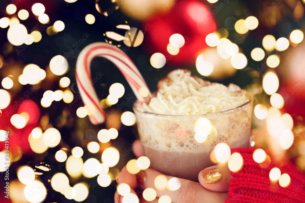 Girl holding cacao with whipped cream and peppermint candy cane. Christmas holiday concept. Holiday background. Festive bold bokeh Girl holding cacao with whipped cream and peppermint candy cane. Christmas holiday concept. Holiday background. Festive bold bokeh
