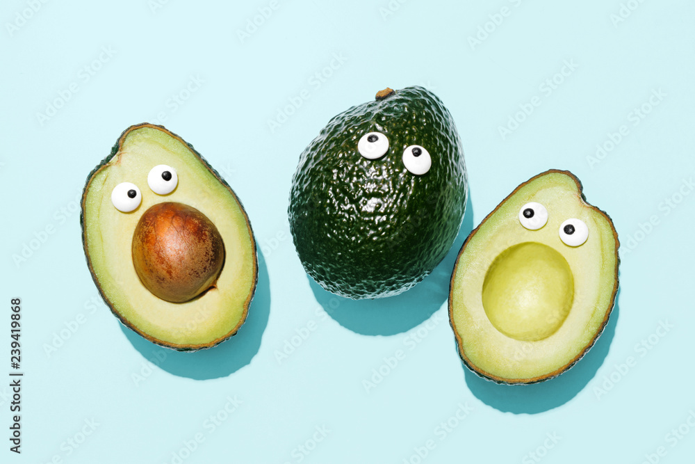 Funny faces avocados on a pastel blue background, creative healthy food concept, top view with clipping path