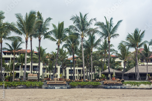 Luxury Hotel, beach resort with large bungalows, sun protection umbrellas by the sea among the palm trees. Bali, Indonesia. Travel concept