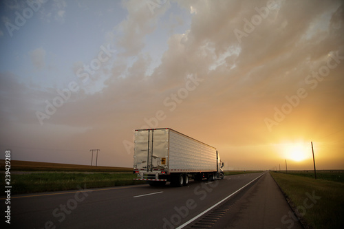 A semi truck drives towards the sunset on a interstate highway