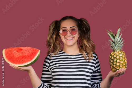 Portrait of cool girl in sunglasses holding the pineapple and slice of watermelon in her hands