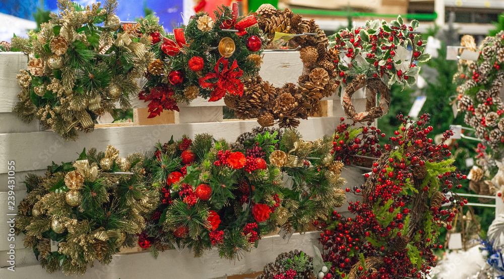 Christmas shopping. Many decorated with red elements and cones green christmas wreaths hanging in store for sale.