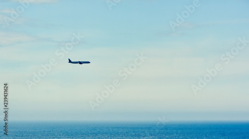 Silhouette of a plane flying against a clean blue sky over the ocean . copy space for text