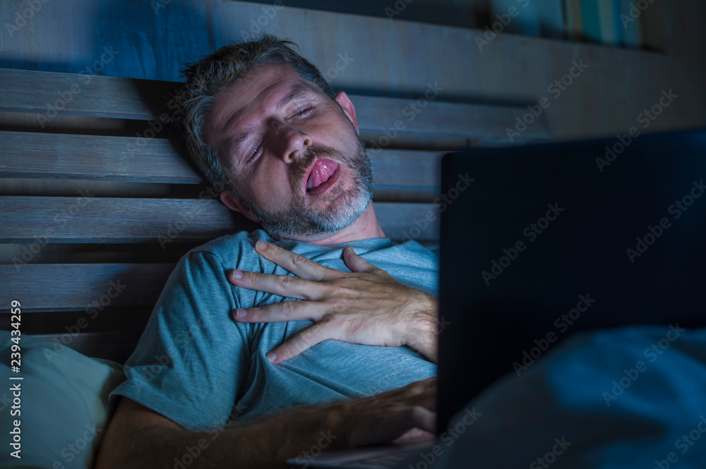 Foto de man alone in bed playing cybersex using laptop computer watching porn  sex movie late at night with lascivious pervert face expression in internet  pornographic sexual content do Stock | Adobe