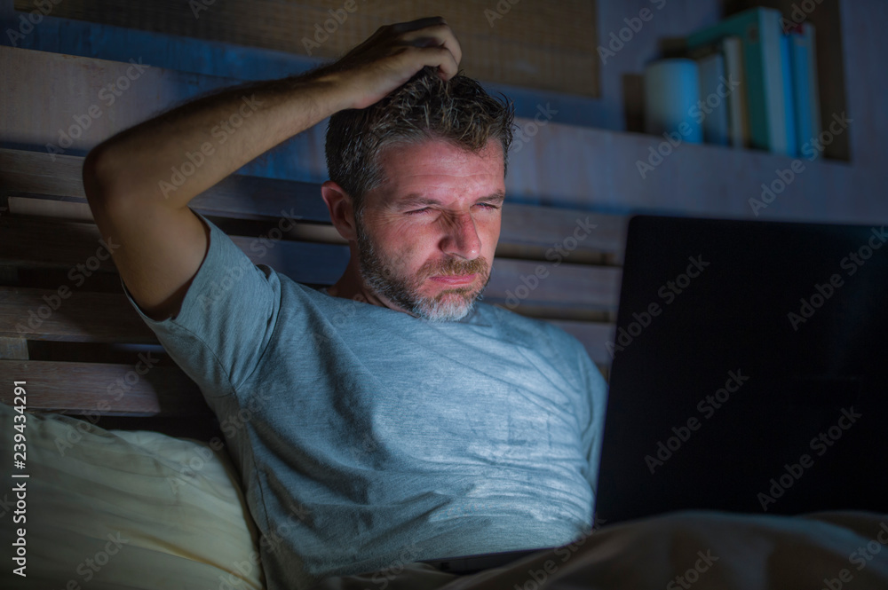 Obraz premium attractive and relaxed internet addict man networking concentrated late at night on bed with laptop computer in social media addiction or workaholic businessman concept