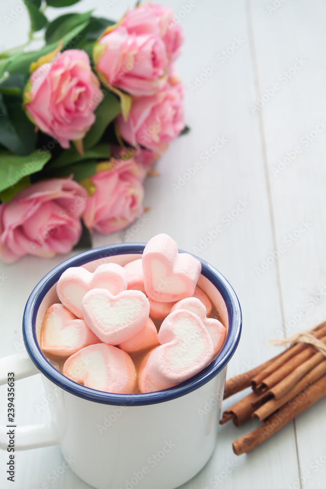 Hot chocolate with heart shape marshmallows on top. Sweet beverage and pink roses on table Hot chocolate with heart shape marshmallows on top. Sweet beverage and pink roses on table