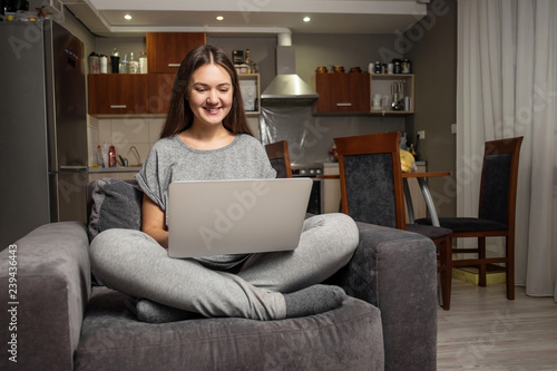 young woman communicates in social networks with laptop, girl sitting at home in chair with laptop