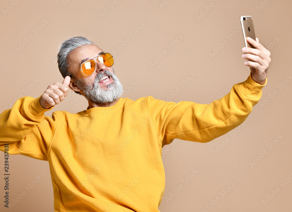 Portrait of happy senior millionaire man using smartphone cellphone make selfie in yellow sunglasses