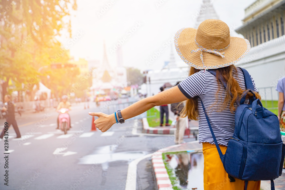 Traveler woman with a backpack hitchhiker beside road. She is show hand hitchhiker after see The Grand Temple Palace in Bangkok ,Thailand.holiday, vacation , Photo Travel and relax time concept. 