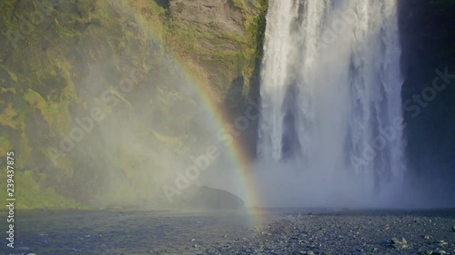 A beautiful slow-motion shot, on a sunny day, of the stunning Sk√≥gafoss waterfall with a rainbow. Medium wide. A very popular tourist attraction in Iceland. photo