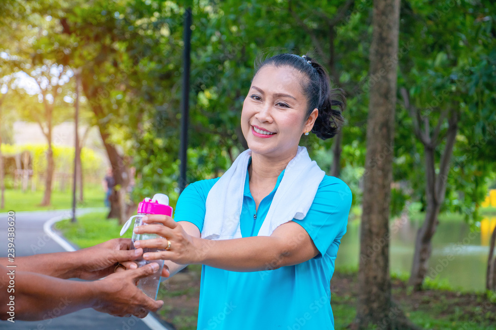 Asian woman relax time in park. A man sent water for woman.She is drinking water.She is  smile and be happy in good time ,Life style,Photo concept  exercise and healthy.