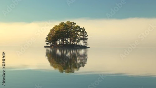 Small lonely island on a lake, foggy morning weather, calm water, perfect water reflections. Moody and calm. photo