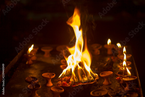 Diwali holiday. a plate with burning flowers in the background of small burning candles in clay stands in the dark.