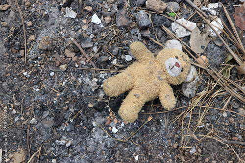 Old dirty teddy bear neglected on the ground soil. End of childhood.