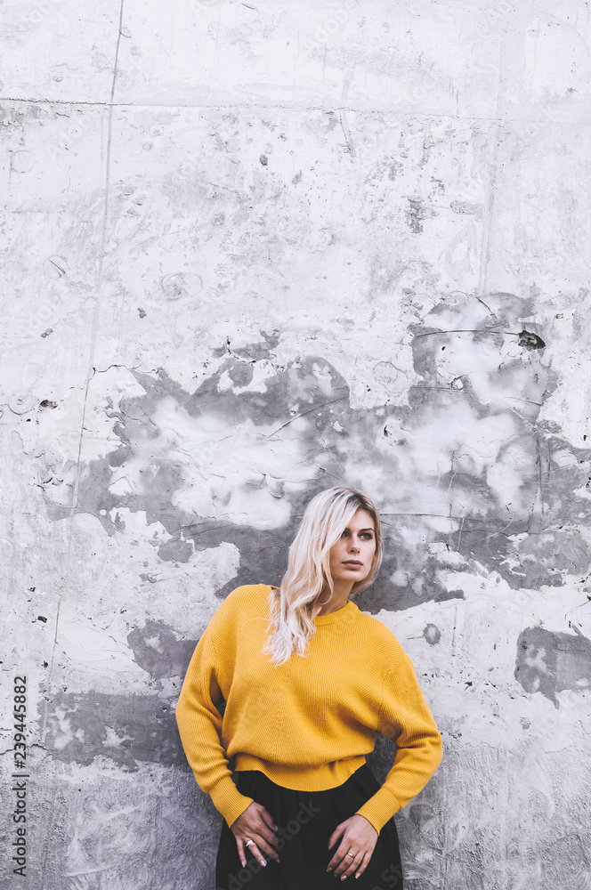 Blond girl in a yellow sweater and in a black skirt against a gray wall background