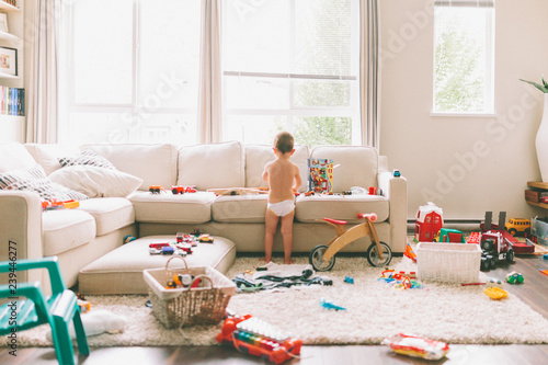 A little boy playing in a messy living room. 