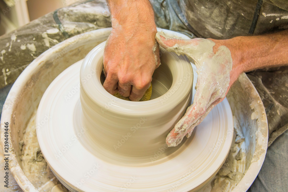     Artist potter in the workshop creating a jug out of earthenware, hands closeup. Twisted potter's wheel. Small aristic craftsmen business concept. 