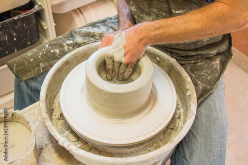  Artist potter in the workshop creating a jug out of earthenware, hands closeup. Twisted potter's wheel. Small aristic craftsmen business concept. 