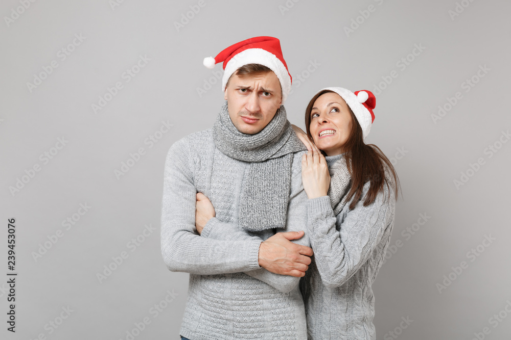 Merry fun couple girl guy in red Santa Christmas hat gray sweaters scarves isolated on grey wall background, studio portrait. Happy New Year 2019 celebration holiday party concept. Mock up copy space. Merry fun couple girl guy in red Santa Christmas hat gray sweaters scarves isolated on grey wall background, studio portrait. Happy New Year 2019 celebration holiday party concept. Mock up copy space.