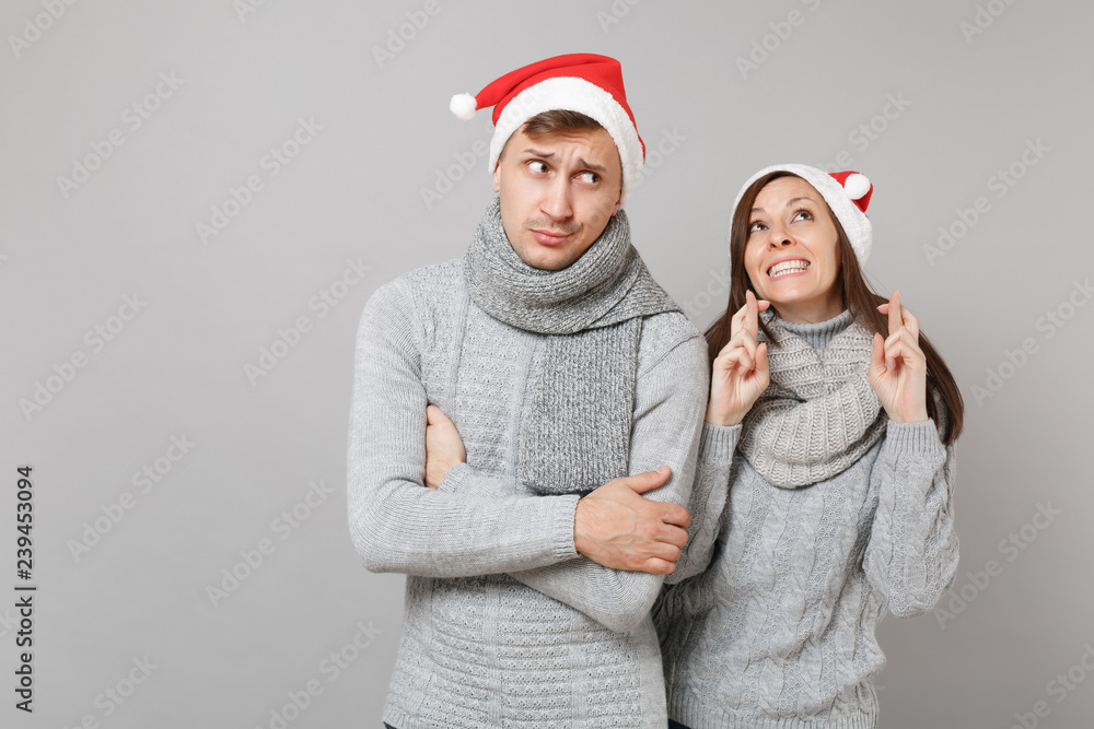 Fototapeta premium Merry fun couple girl guy in red Santa Christmas hat gray sweaters scarves isolated on grey wall background, studio portrait. Happy New Year 2019 celebration holiday party concept. Mock up copy space.