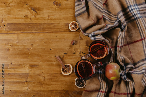 Mulled wine in mugs with scarf on wooden table.