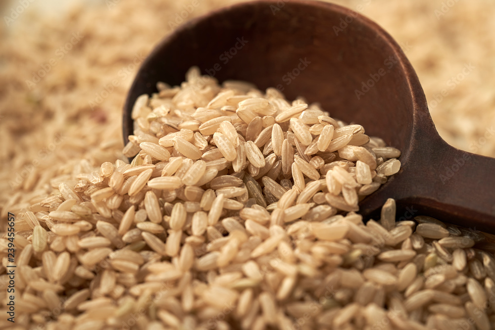 Obraz premium Macro photo of brown rice with a wooden brown spoon on a linen cloth background. Close up of brown rice scooped with a wooden brown spoon.