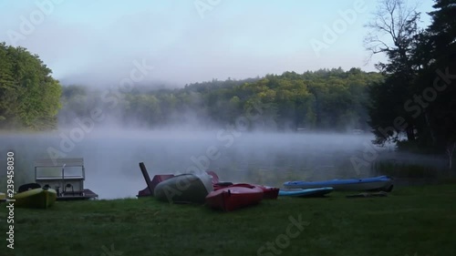 Canoes and kayaks at a pond with early morning mist floating over water.