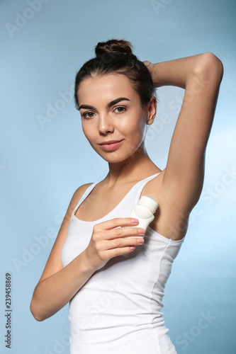 Young woman using deodorant on color background