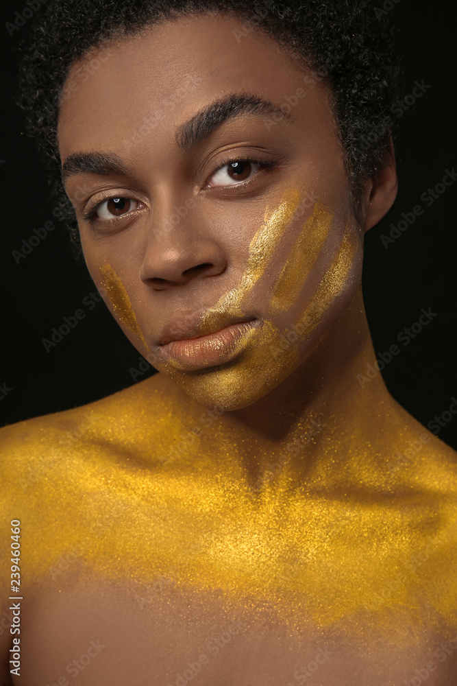 African-American woman with golden paint on her body against black background African-American woman with golden paint on her body against black background