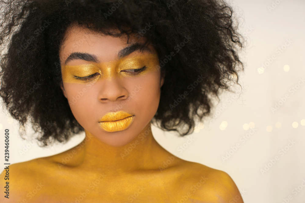 African-American woman with golden paint on her body against light background African-American woman with golden paint on her body against light background